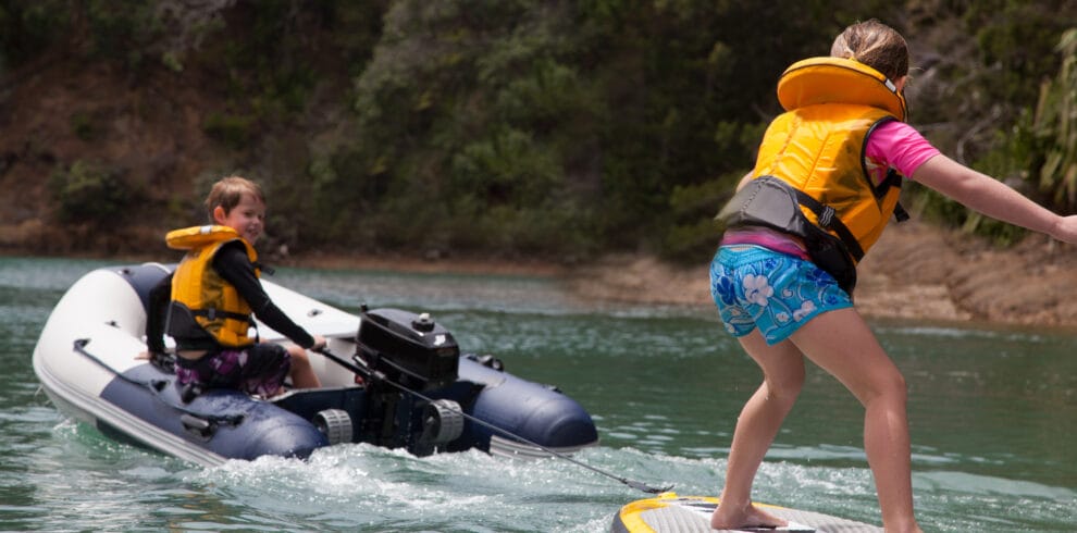 Brother in motor dinghy towing sister standing on paddleboard