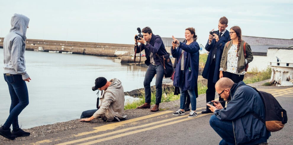 Friends photographing woman walking road by river against sky
